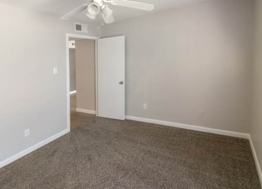 a spacious bedroom with plush carpeting and a ceiling fan with a light kit