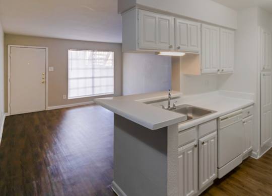 a kitchen with white cabinets and appliances and a living room with wood-style flooring and a large window