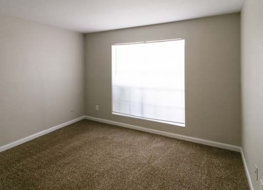 a carpeted bedroom with a large double window at The Forest Apartments