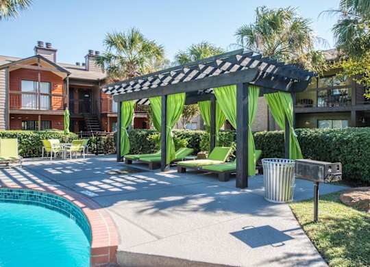 a pergola with loungers, and curtains, and a poolside grill at Hudson at Westchase