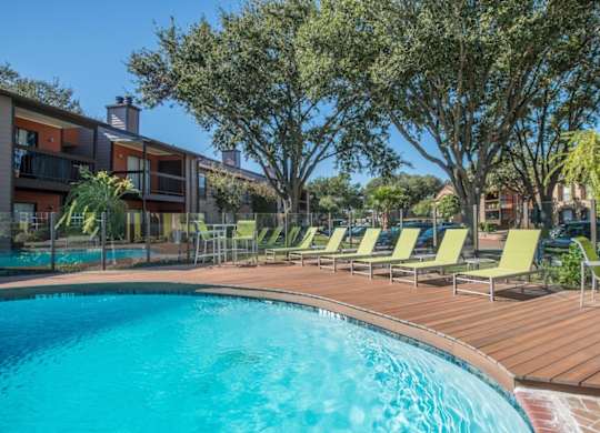 a crystal blue swimming pool surrounded by green lounge chairs and lush trees