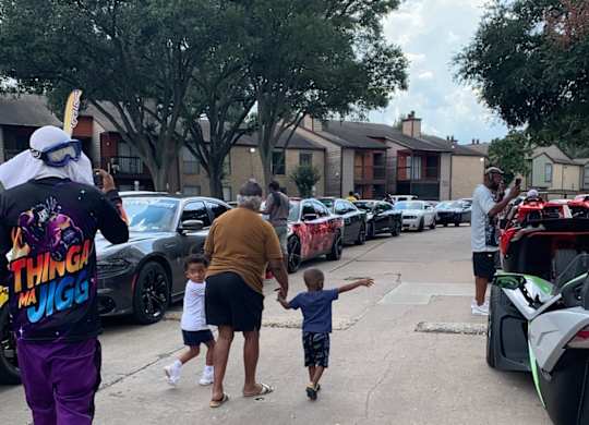 A man in a purple outfit is holding hands with a child while walking in a parking lot.