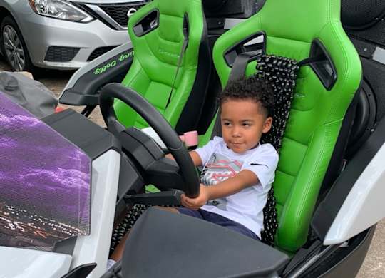 A young child is sitting in a green and black racing simulator.