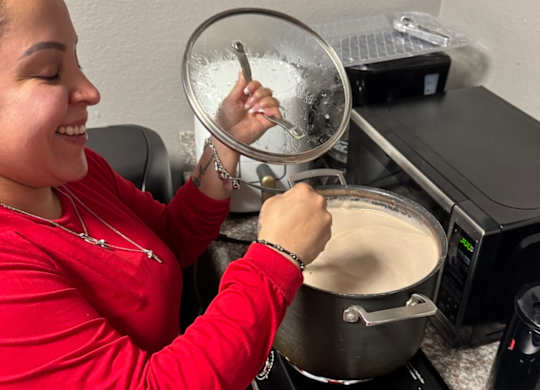 A woman in a red shirt is stirring a pot with a ladle.