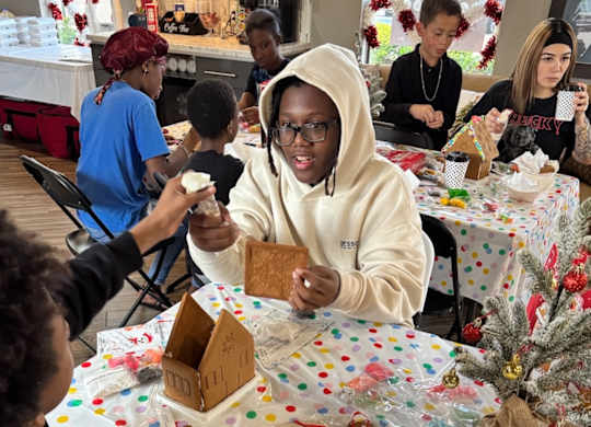 A person in a white hoodie is decorating a gingerbread house.