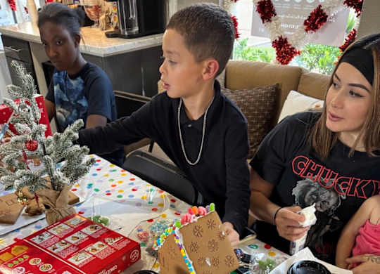 A boy is decorating a Christmas tree with a girl and a woman watching him.
