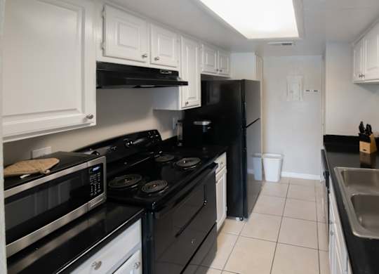 a kitchen with tiled floor, black appliances, and white cabinets