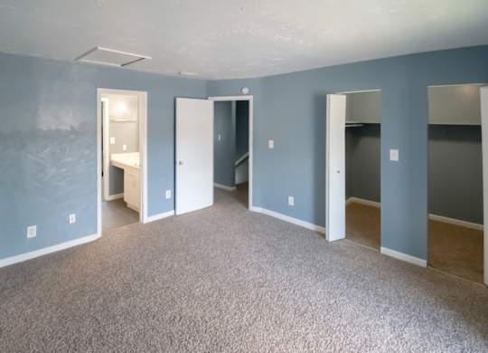 a Winford Place bedroom with blue walls, carpet, and spacious closets with built in shelving