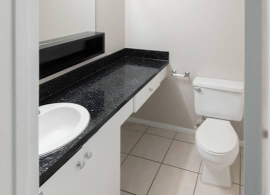 A mirror, large black sink vanity, and a toilet in a tiled bathroom