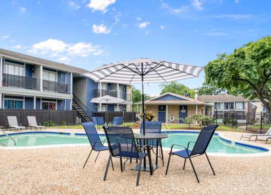 one of the two pools with a large sundeck, table, chairs, and umbrella at Pine Creek Apartments