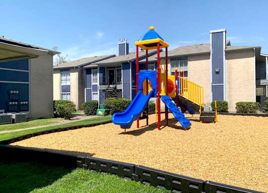 A playground with a blue and yellow slide at Pine Creek Apartments in Houston, TX
