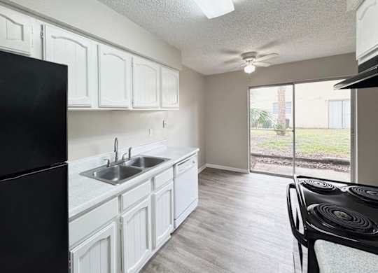 A black refrigerator stands next to a white sink in a kitchen.