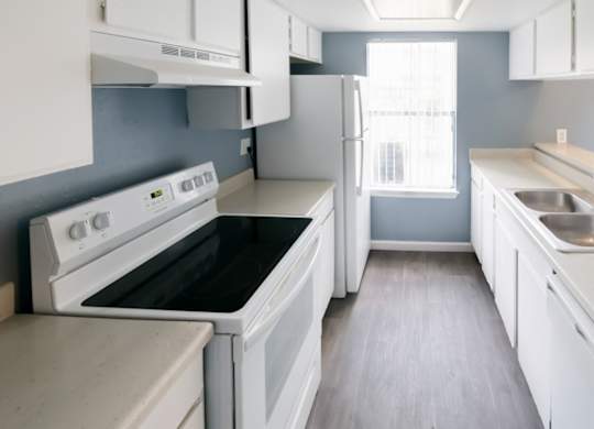 a large kitchen with efficient white appliances, white cabinets, and wood-style floors