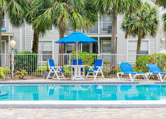 a swimming pool with blue chairs and an umbrella in front of a building