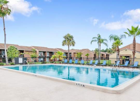 a swimming pool, sundeck, and lots of lounge chairs surrounded by tall palm trees