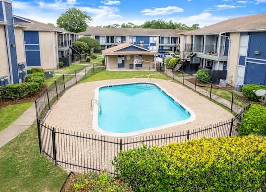 A small pool surrounded by a black fence and green bushes. at Pine Creek Apartments, Texas