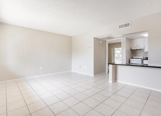 a spacious living room and kitchen with a tiled floor and lots of natural light