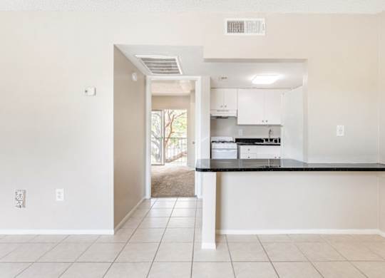 a living room and kitchen with a tiled floor, black countertops, white cabinets, and overhead lights