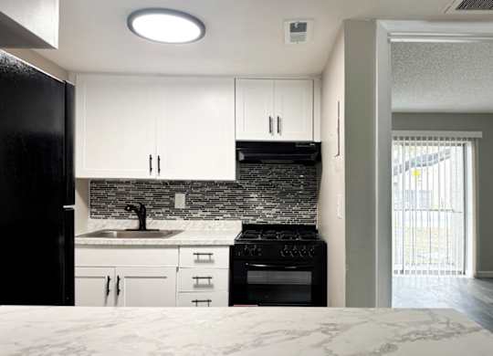 A kitchen with black appliances, tile backsplash, and white cabinets.