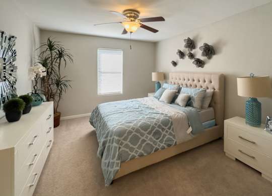a bedroom with plush carpeting, an illuminated ceiling fan, a window, and model furniture