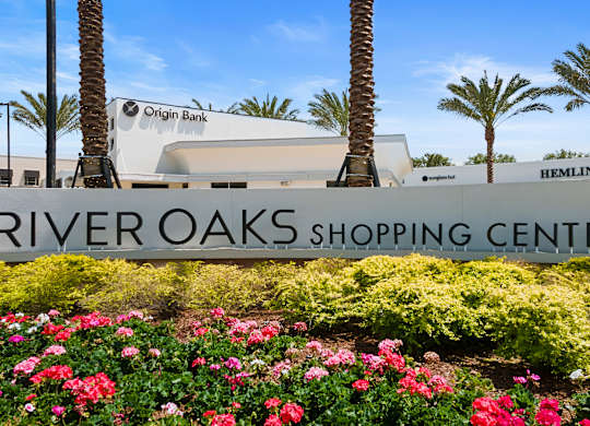 A shopping center named River Oaks Shopping Center is surrounded by palm trees and has a sign for Origin Bank.