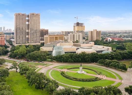 A cityscape with a green park in the foreground and a tall building under construction in the background.