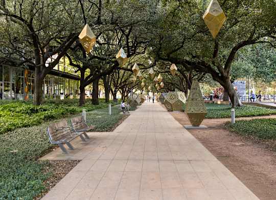 A walkway with benches and hanging sculptures is lined with trees.