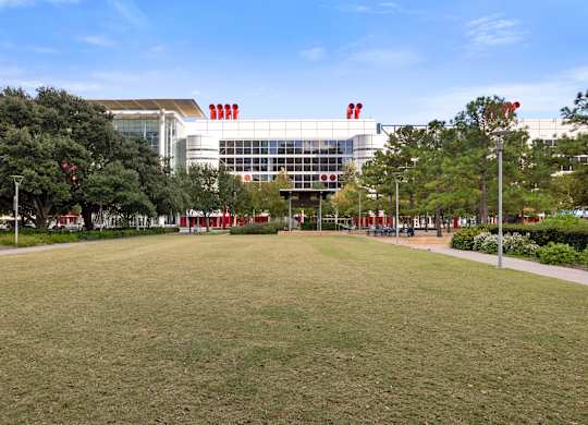 A large building with a glass facade and red accents sits behind a grassy area with trees.