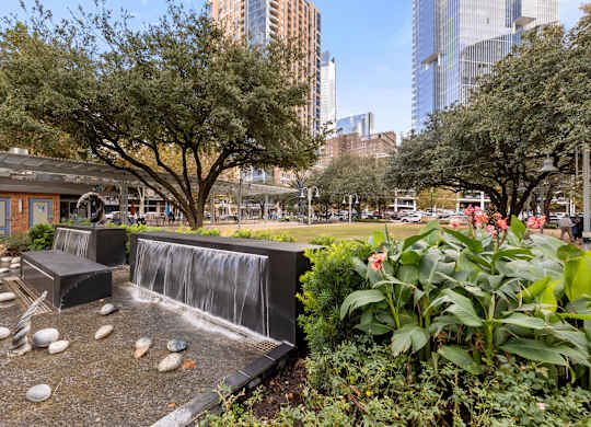 A small waterfall in a garden with a city skyline in the background.