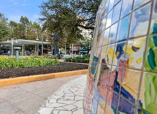 A colorful mosaic wall is in the foreground of a park with a walkway and trees.