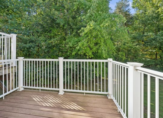 a deck with white railing and trees in the background