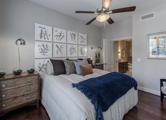 A bedroom with a bed, a ceiling fan, and a wall with pictures.