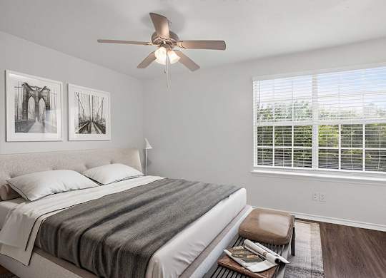 A bedroom with a bed, a ceiling fan, and two framed pictures on the wall.