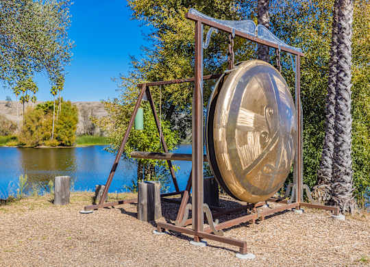 A large gong sits on a stand by a body of water.