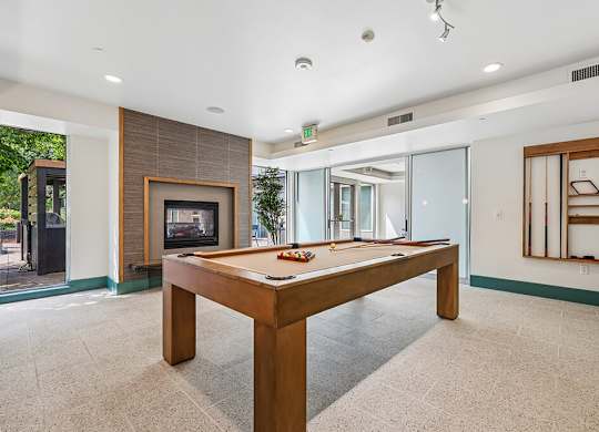 A billiard table in the middle of a room with a fireplace and sliding glass doors.