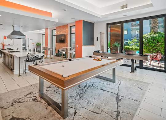 A billiard table is in the middle of a room with a kitchen area.