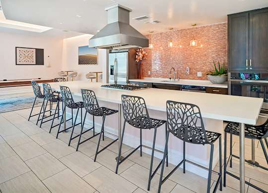 A kitchen with a long white island and black chairs.