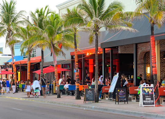 A street view of a busy area with palm trees and people walking.