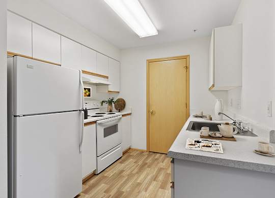 Kitchen with a white refrigerator freezer next to a stove top oven at Lakewood Meadows Apartments in Lakewood WA