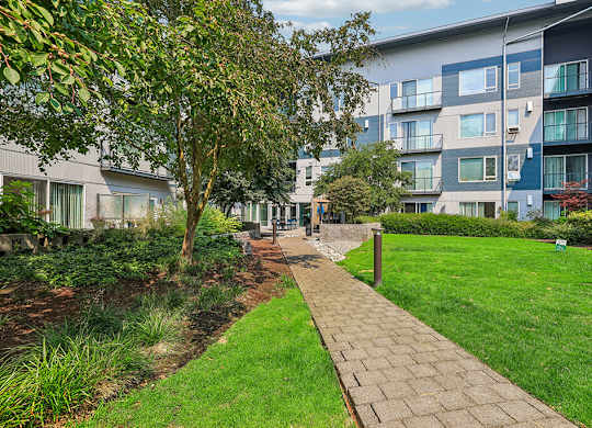 A walkway leads through a grassy area between two apartment buildings.