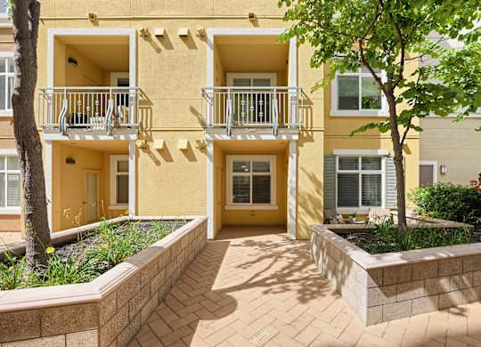 A yellow apartment building with a balcony and a small garden in front.