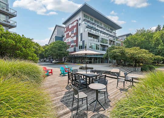 A wooden deck with chairs and tables is surrounded by greenery.
