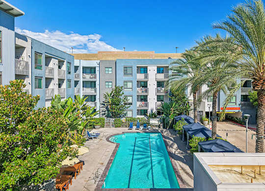 A swimming pool in front of a building surrounded by palm trees.