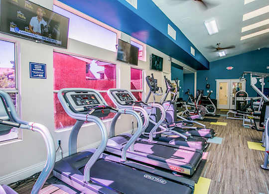a gym with cardio equipment and a large screen tv