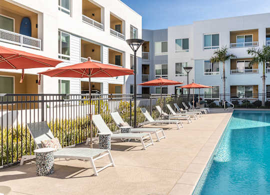 A pool area with red umbrellas and lounge chairs.