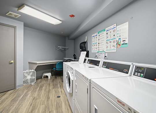 A laundry room with washers and dryers and a fan.
