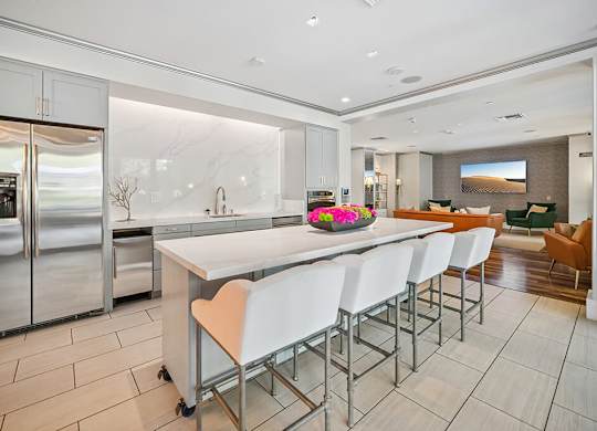 A modern kitchen with a long white island and stainless steel appliances.