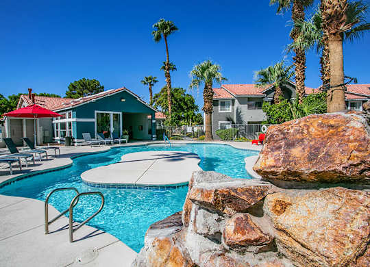 a swimming pool with a stone wall and chairs around it