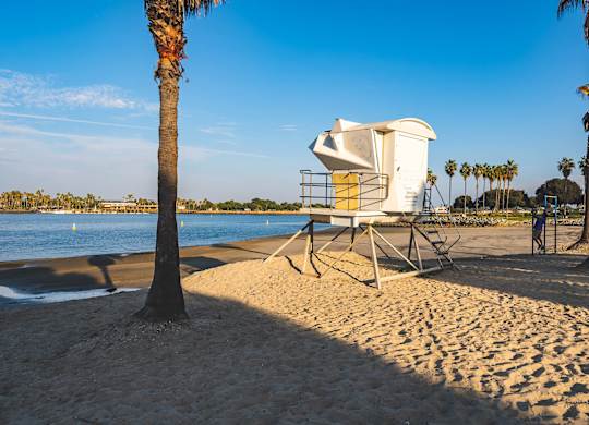 A lifeMission Bay Lifeguard Tower Near The Seaton Apartment in San Diego CAguard tower sits on a beach with a palm tree in the foreground.