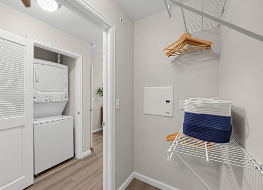 A laundry room with a washer and dryer, a basket on a rack, and a hanger with clothes.